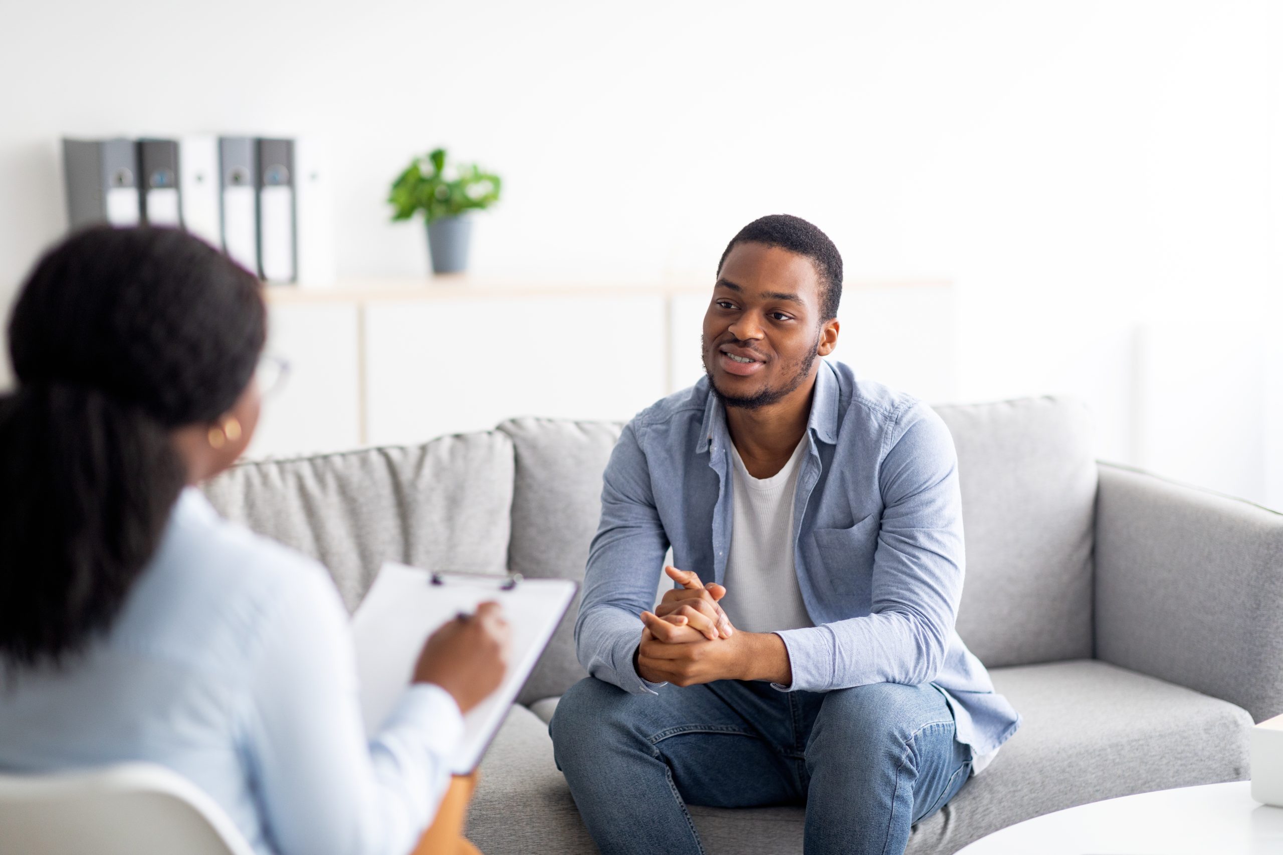 Effective psychotherapy. Young black guy talking to his psychologist, receiving professional help at mental health clinic. African American male patient sharing therapy results with counselor