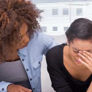 Sad woman crying next to her therapist who is comforting her
